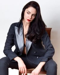 Picture of brunette lady wearing black classic suit and has red lips, sitting on chair and looking away, pretty female looks confident, posing isolated over white studio background, elegance girl.